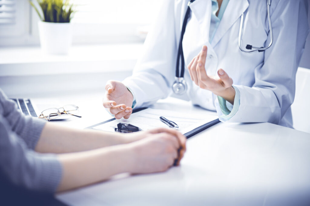 Doctor and female patient sitting at the desk and talking  in clinic near window. 