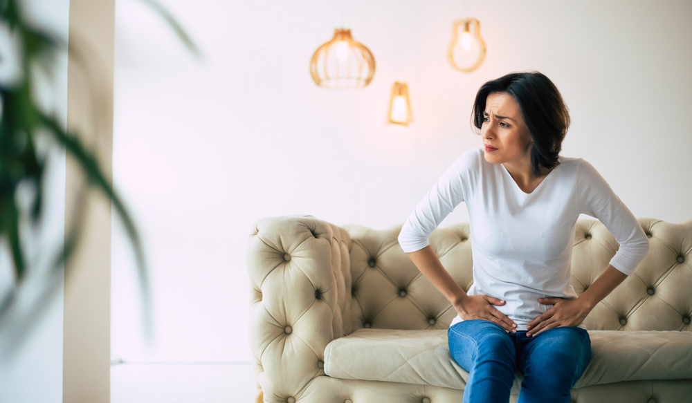 Woman sitting on a sofa and holding her abdomen with painful expression